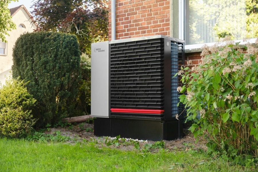Buitenunit van een warmtepomp naast een bakstenen muur
